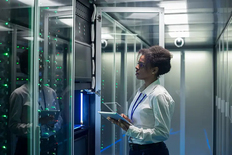 Female technician working on a tablet in a data center full of rack servers running diagnostics and maintenance on the system