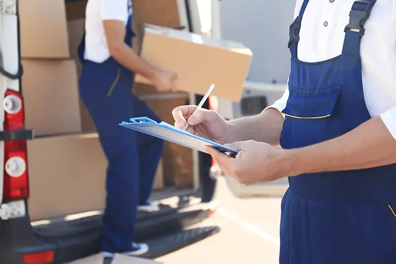 Delivery man from removal company checking list on clipboard near van