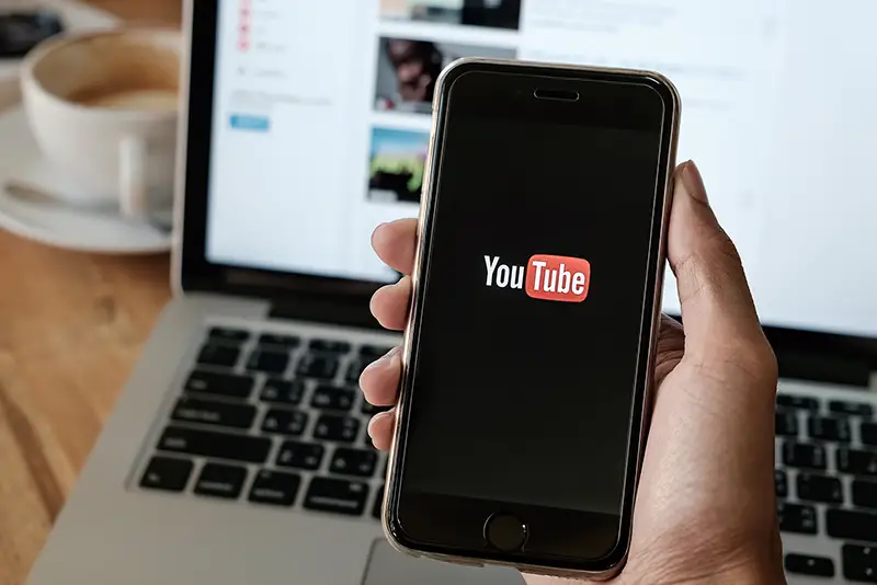 Man hands holding a Iphone 6s mobile phone which displays the Youtube app on the touch screen.