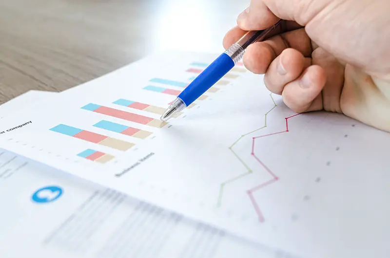 Person holding blue ballpen pointing on paper with colorful chart print