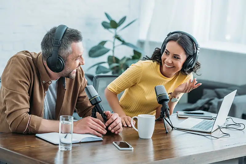 two radio hosts in headphones laughing while recording podcast in studio together