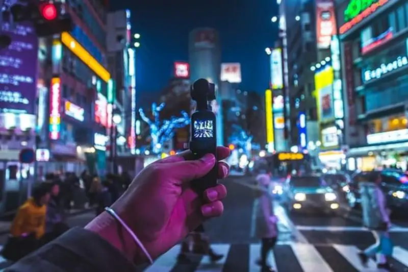 Man holding vsmall black video cam on the street at night time