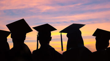 Silhouettes of students with graduate caps in a row on sunset background.