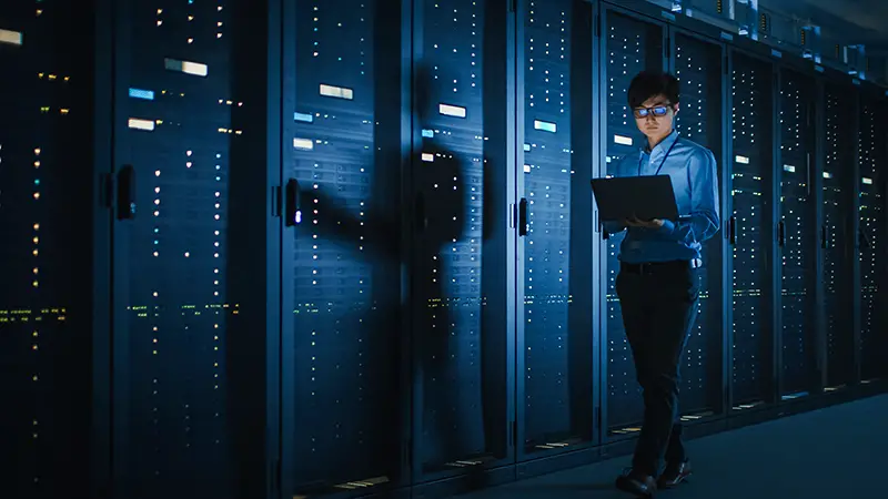 Male IT Specialist Walks along the Row of Operational Server Racks