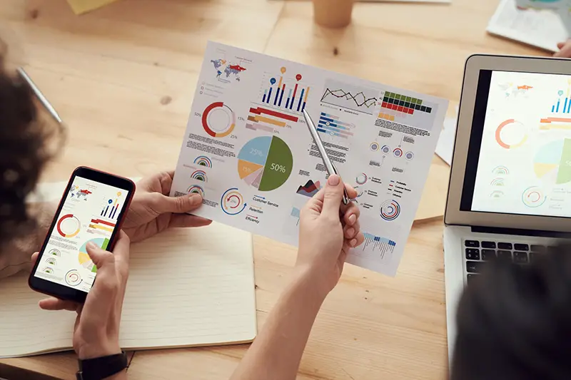 two people looking and data charts - one holding a mobile phone