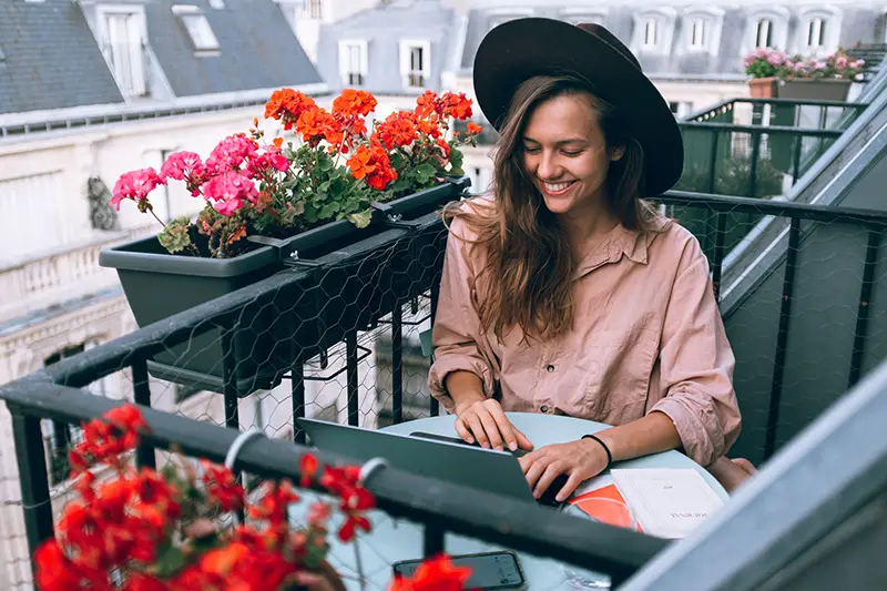 Happy woman wearing dark brown hat while working on her laptop