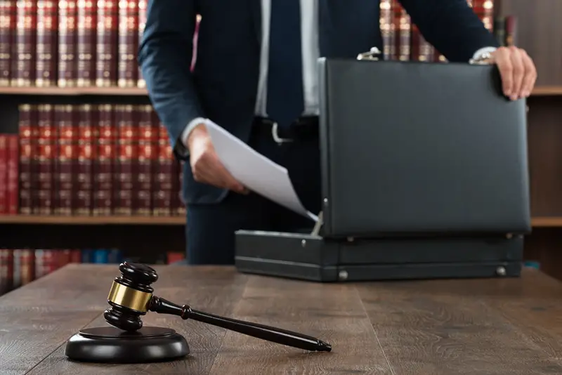 Midsection of lawyer putting documents in briefcase with gavel at desk in courtroom