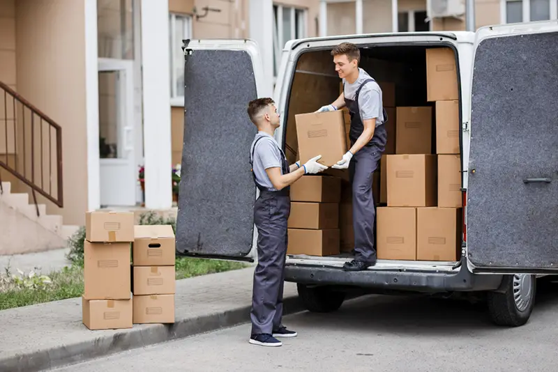 Two young handsome movers wearing uniforms are unloading removal van