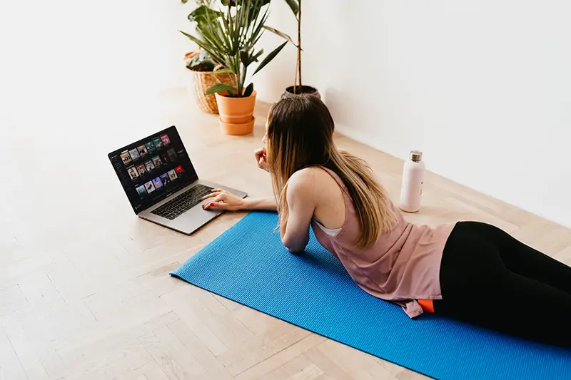 Young woman lying on floor on mat while doing the online training