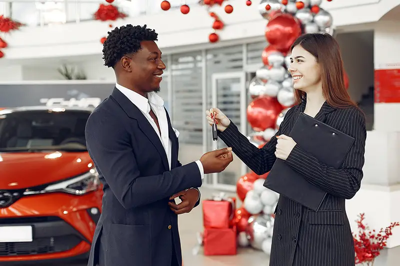 Young preety car loan agent handing the car key to her cclient