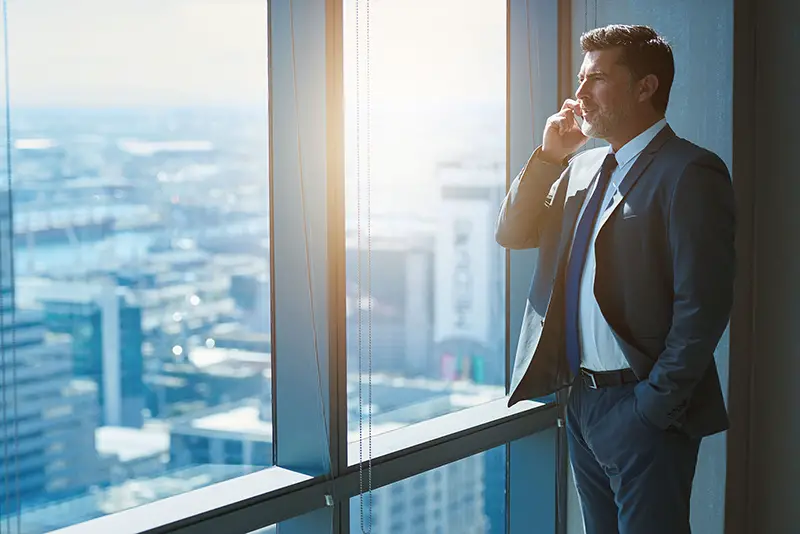 Businessman standing near the glass window while talking on phone