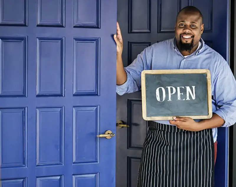 Man standing beside blue door holding open signage