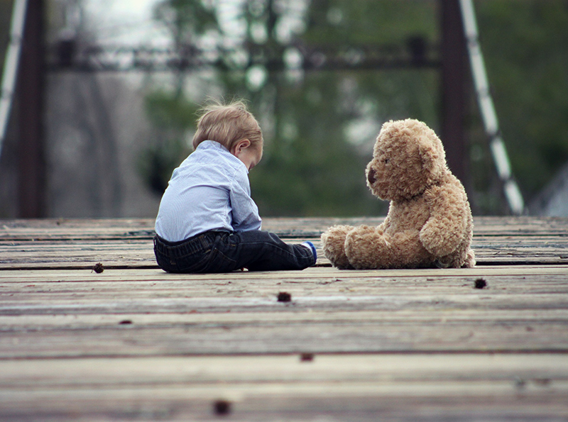 young boy sitting with brown bear plush toy on wooden bridge