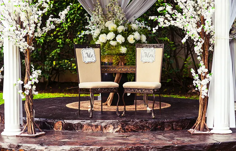 Wedding chairs for Mr and Mrs in outdoor setting with pillars and drapes