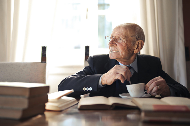 elderly gentleman drinking a hot beverage while sitting at a table with books