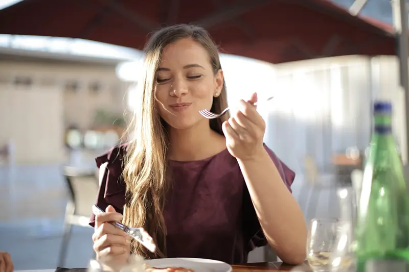 Young woman wearing maroon blouse eating outside restaurant