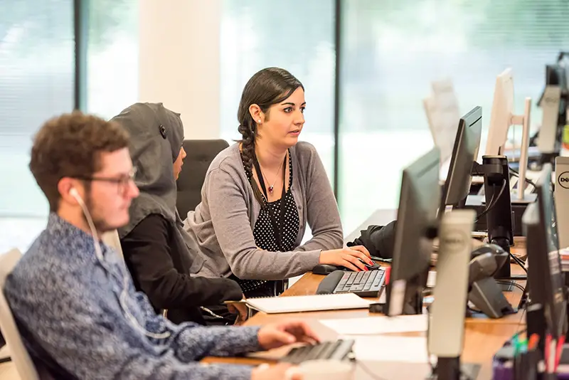 people working in an office at their desks and computers