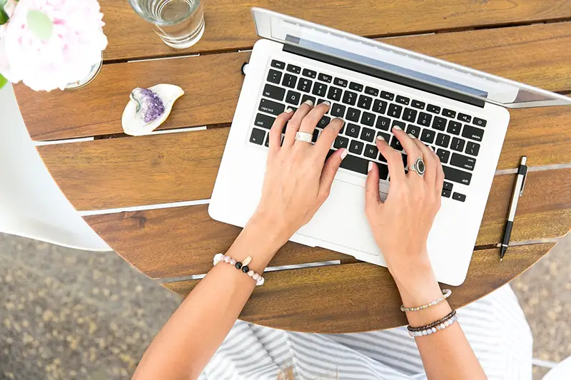 Person typing on laptop on top of brown wooden table