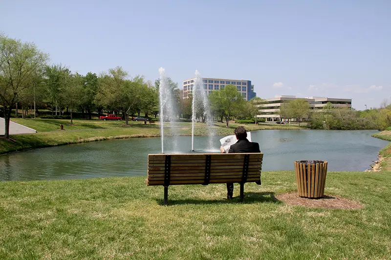 Person reading newspaper on bench in park near pond and fountain