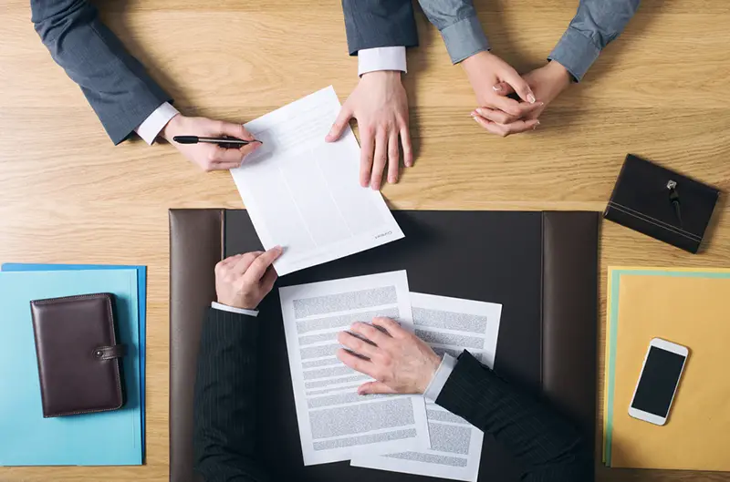 Business man and woman sitting at independent agents office desk and signing important documents, hands top view