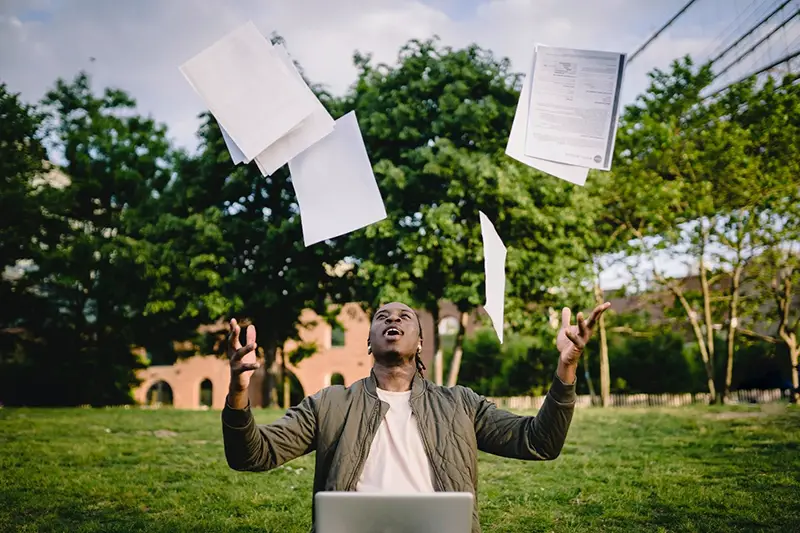 Man sitting in front of his laptop while throwing out documents