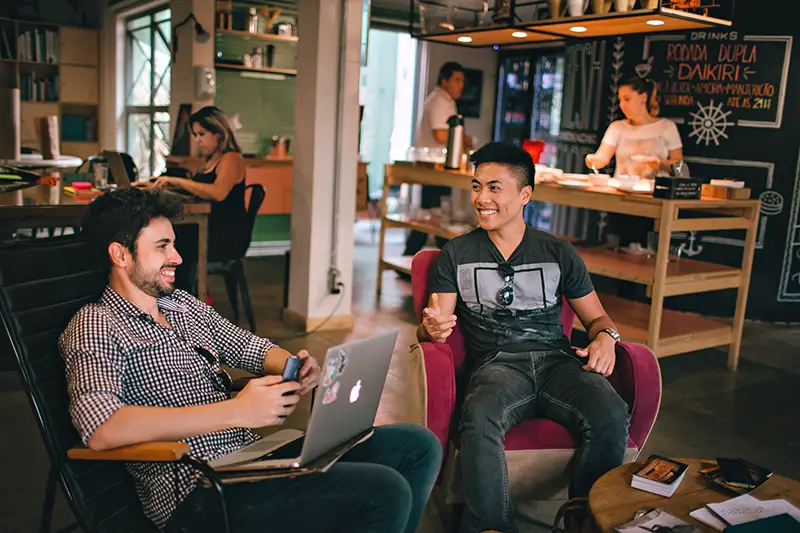 Men sitting in a coffee shop having a conversation and one working on a laptop