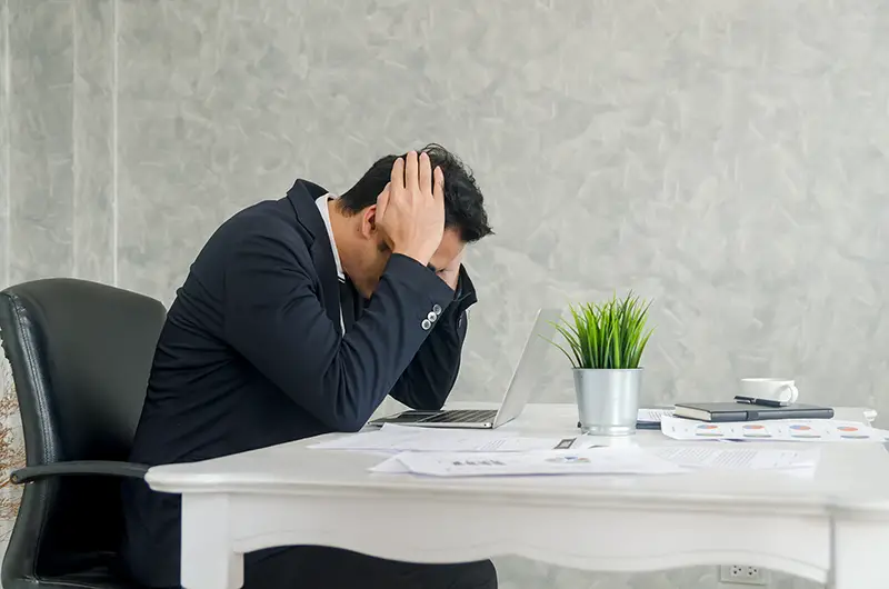 Stressed businessman in suit sitting at office with burnout syndrome at desk.