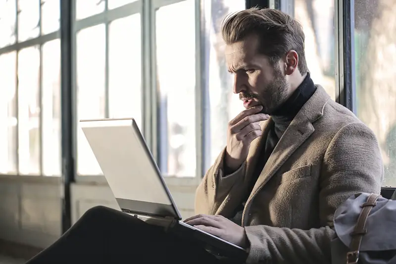 Man holding his chin while facing on his laptop