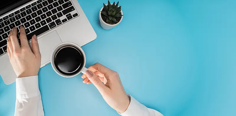 Freelancer working on laptop and holding cu of coffee