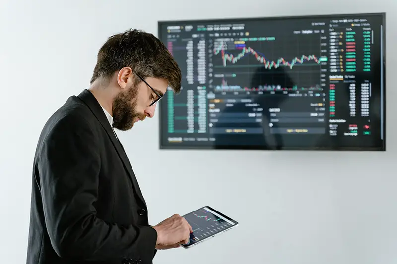 Man in black suit in front of screen with graph