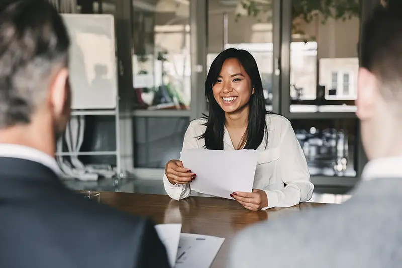 young asian woman smiling and holding resume, while sitting in front of directors during corporate meeting or job interview