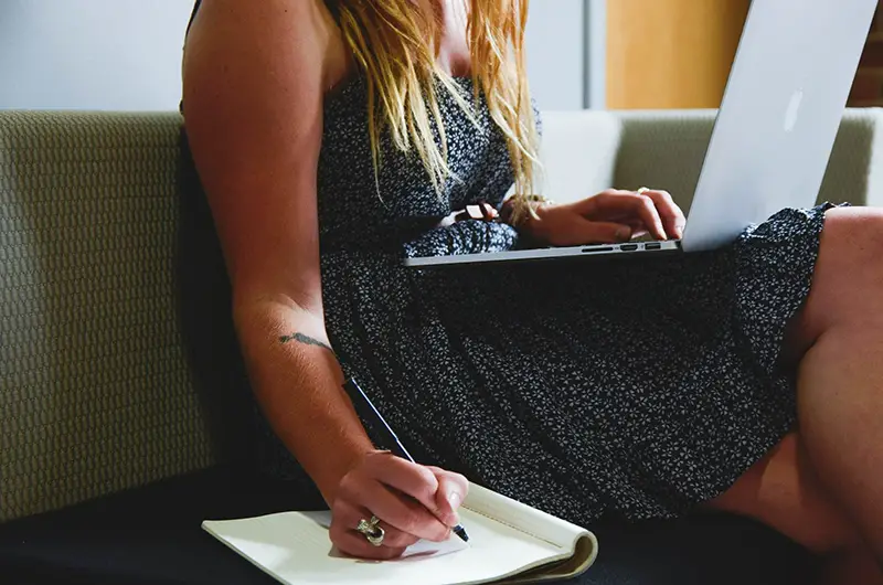 Entrepreneur making notes in notepad - laptop on lap