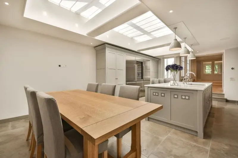 A large kitchen with a wooden table and grey cabinets and skylights above