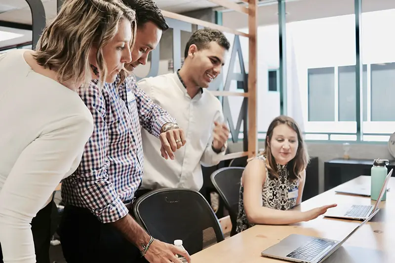 members of a team looking at a computer - three standing and one seated