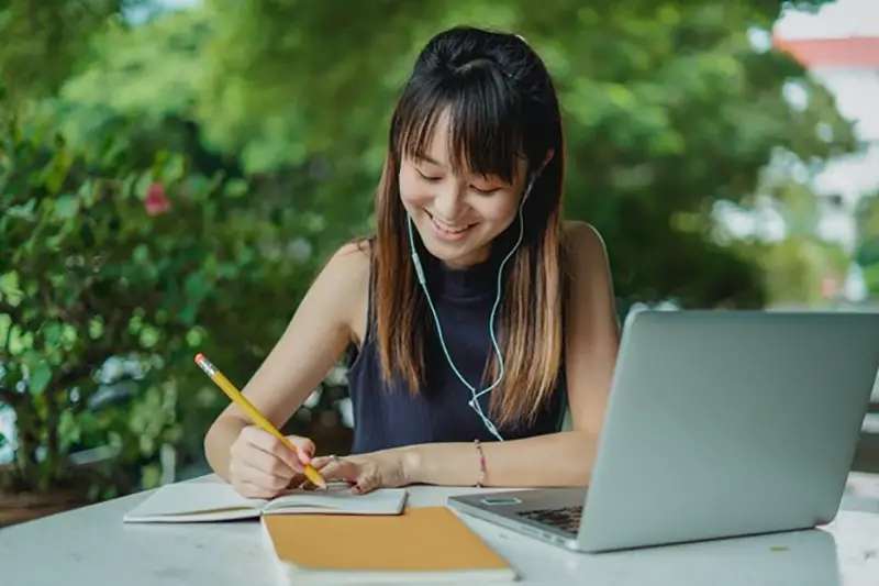 Young asian girl writing on her notepad while wearing headset