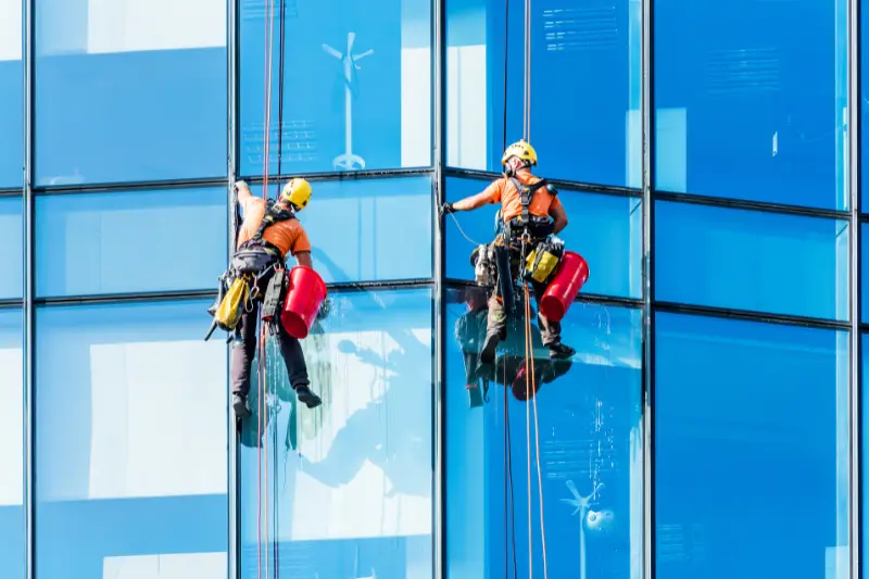 Window cleaner working on a glass facade of modern skyscraper.