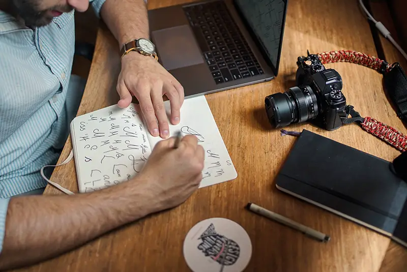 Man sketching a logo on paper near DSLR camera