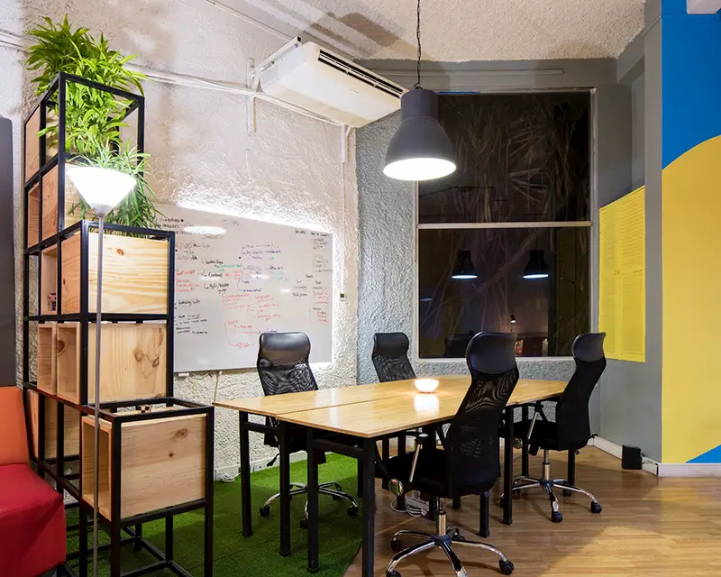 Startup office with desk, and black chairs. Whiteboard beneath HVAC system on the wall.