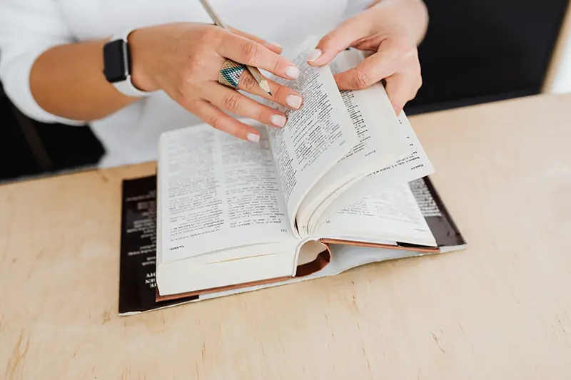 Person wearing silver ring holding white book page