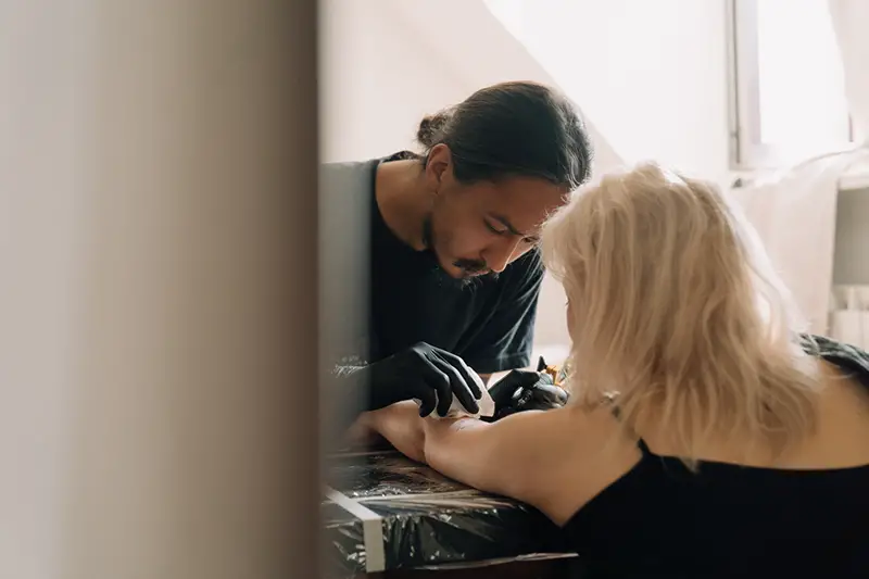 Man in black shirt putting tattoo in woman left arm