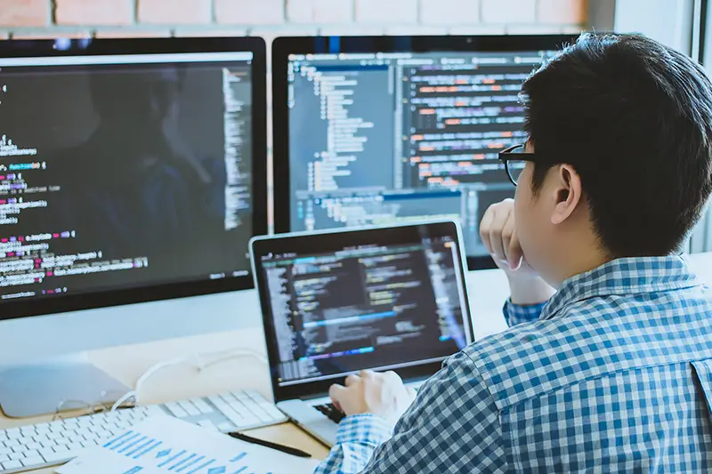 IT specialist in front of computer screen and laptop