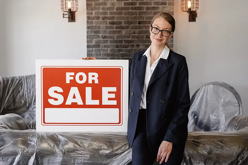 Woman wearing black suit and eye glasses holding for sale banner