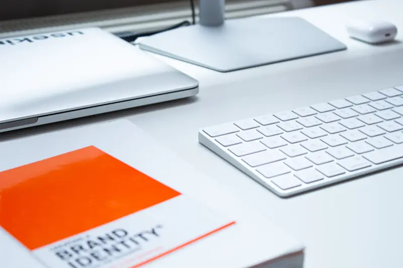 brand identity book on white desk next to laptop, keyboard and monitor
