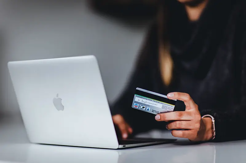 Woman holding credit card in front of silver Macbook