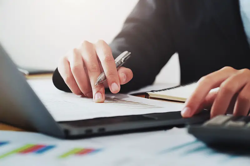 close-up hand of businessman analyzing investment chart on paperwork with laptop in office. concept finance and accounting