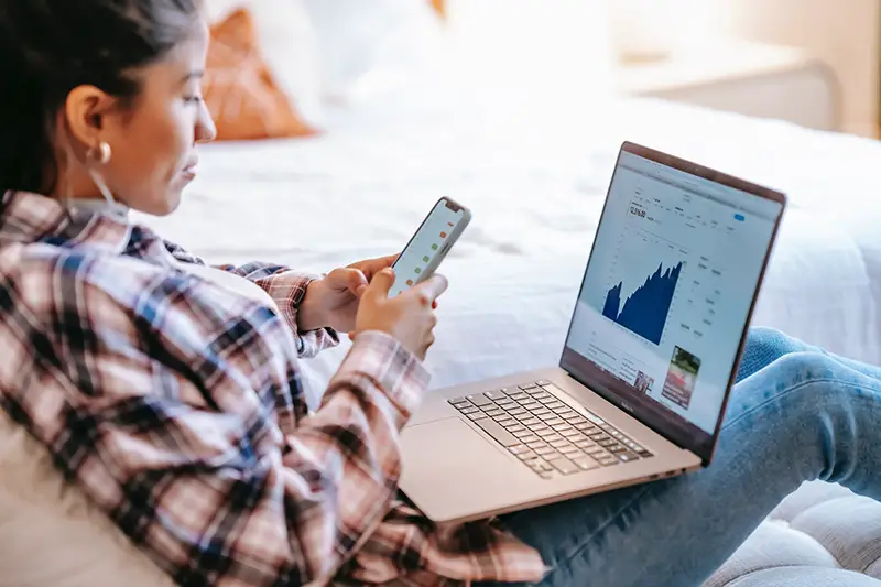 Woman using smartphone with laptop on her front