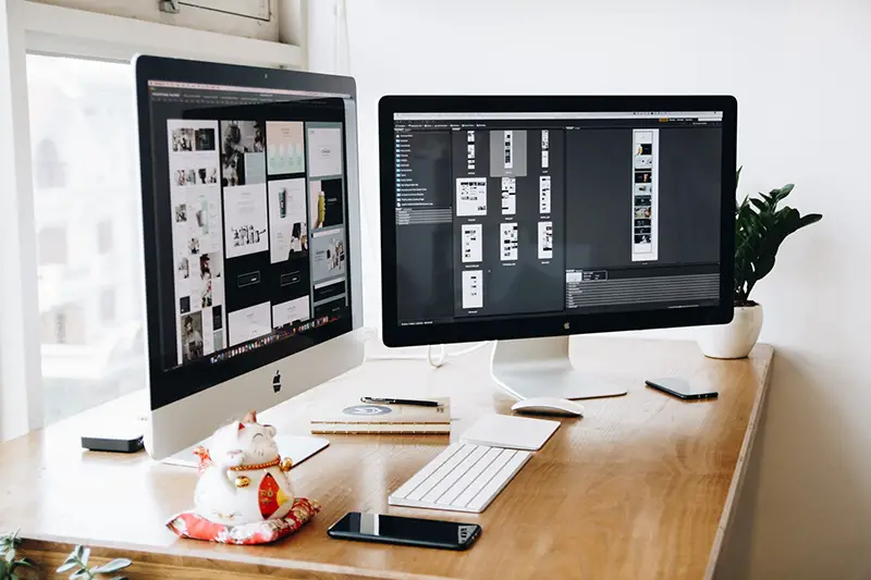 Two Imac with keyboard and phones on desk