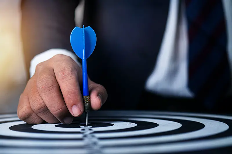 Businessman holding blue dart pin pointing to dartboard