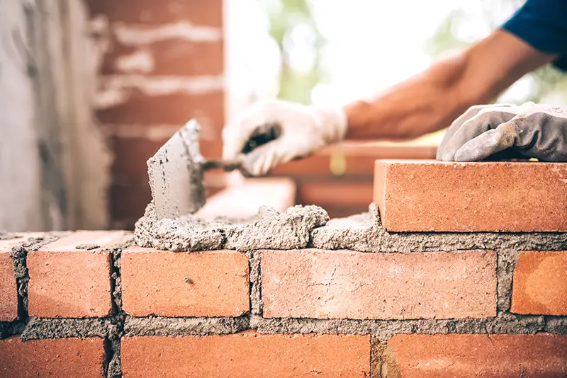 Bricklayer worker installing brick masonry on exterior wall