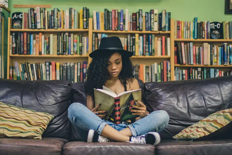 young woman with black hat reading books in the couch